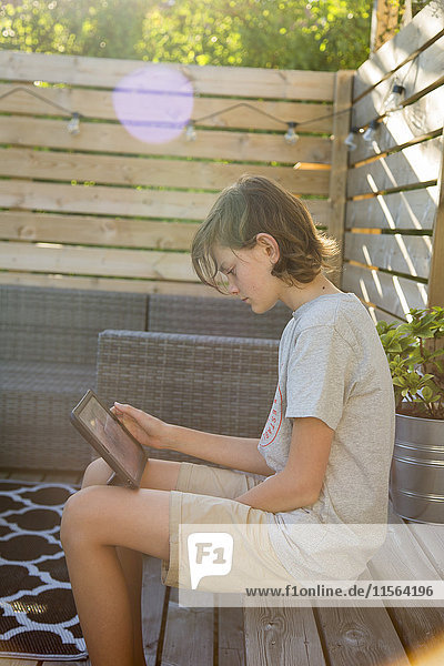 Sweden  Boy (14-15) using tablet on wooden terrace