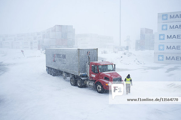 Ein Fahrer geht während eines Schneesturms zu seinem Lkw von Horizon Lines im Containerhof  Unalaska  Südwest-Alaska  USA