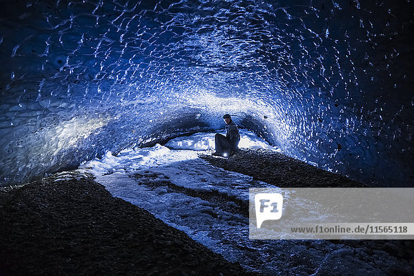 Ein Mann beleuchtet das Ende eines dunklen  langen Tunnels im Eis des Canwell-Gletschers in der Alaska Range.