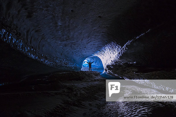 Ein Mann steht in einem langen Tunnel im Eis des Canwell-Gletschers in der Alaska Range.