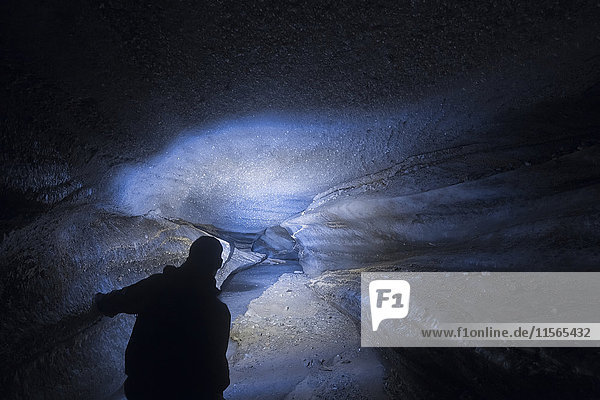 Ein Mann leuchtet mit seiner Stirnlampe in das Innere eines langen Tunnels im Castner Glacier in der Alaska Range; Alaska  Vereinigte Staaten von Amerika'.