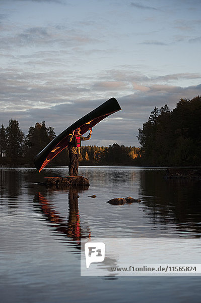 Schweden  Smaland  Erwachsener Mann auf Felsen im See stehend und Boot haltend
