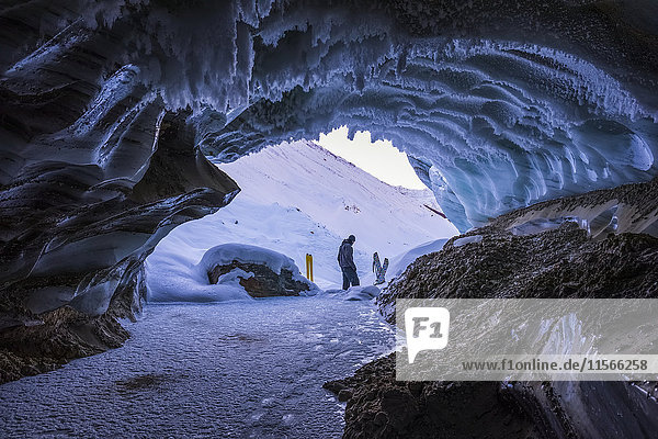 Ein Mann lauscht dem Wasser  das unter dem Schnee vor dem Eingang einer Höhle des Castner-Gletschers in der Alaska Range fließt; Alaska  Vereinigte Staaten von Amerika'.