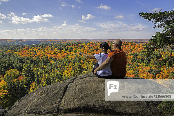 'Young couple siting on a clifftop looking at the autumn colours of Algonquin Park; Ontario  Canada'
