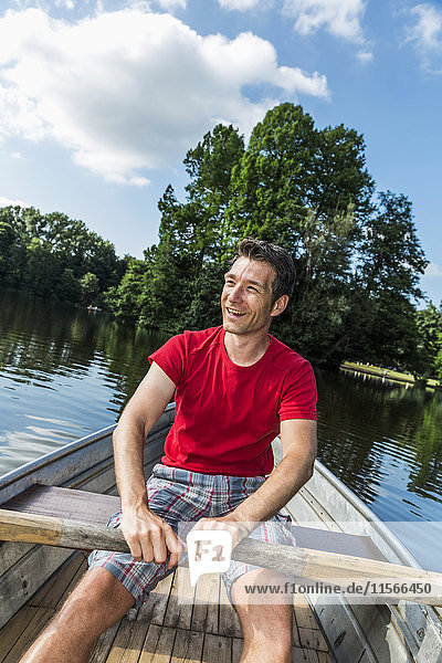 'A smiling man rowing a boat down a calm river on a clear sunny day; Darmstadt  Hessen  Germany'