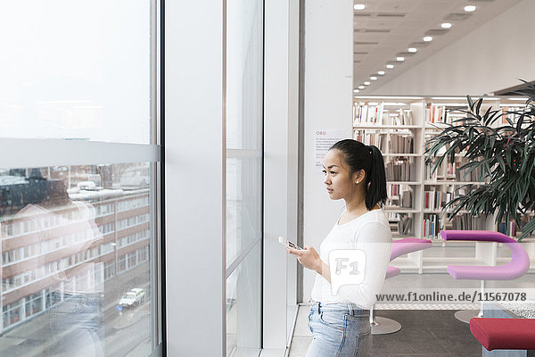 Junge Frau schaut durch ein Fenster in einer Bibliothek