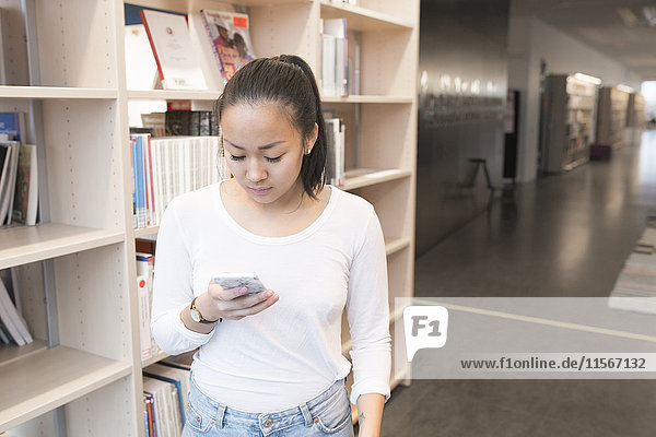 Junge Frau benutzt Mobiltelefon in der Bibliothek