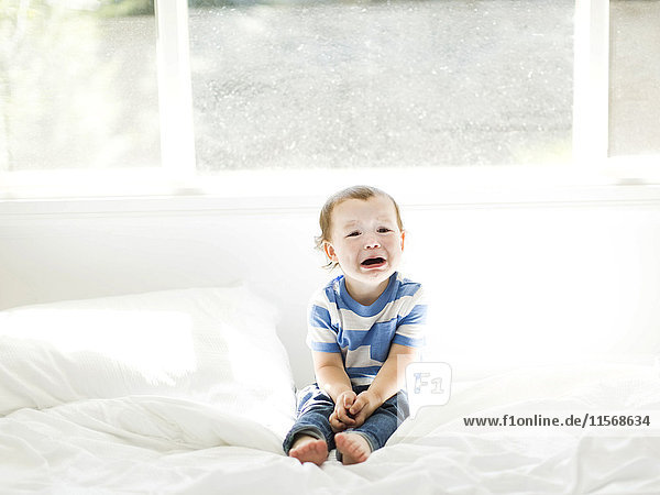 Boy (4-5) sitting on bed and crying