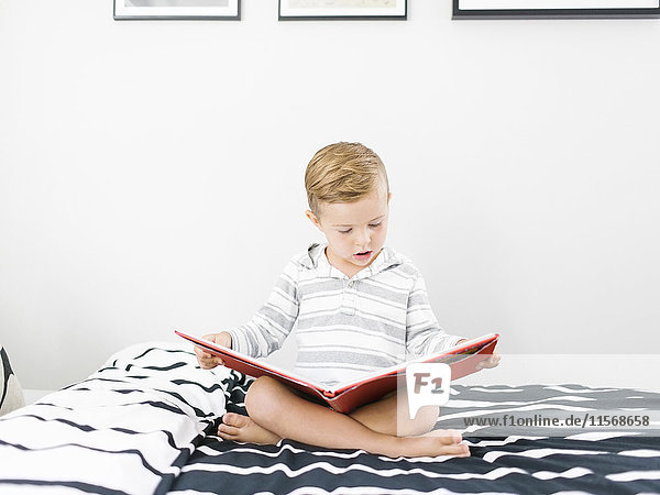 Boy (4-5) sitting on bed and reading book