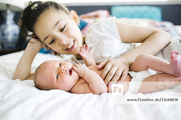 Girl (10-11) lying in bed beside brother (2-5 months)