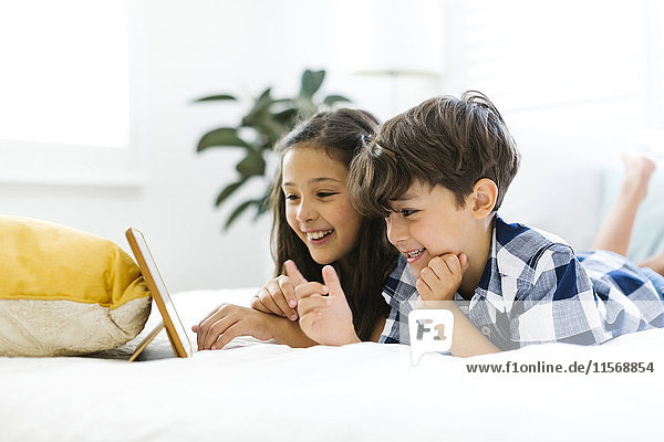 Siblings (10-11  6-7) lying in bed and using tablet