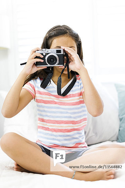 Sitting girl (10-11) holding camera and taking photo