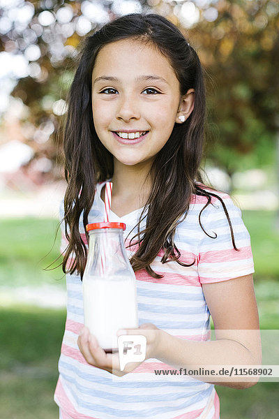 Mädchen (10-11) im Park hält ein Glas Milch mit Strohhalm