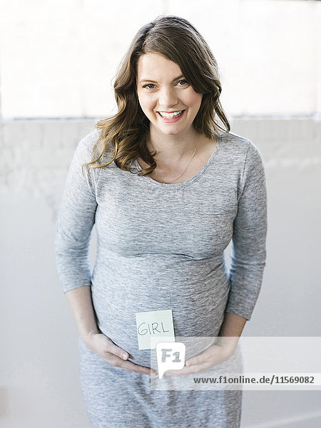 Portrait of smiling pregnant woman with adhesive note on belly
