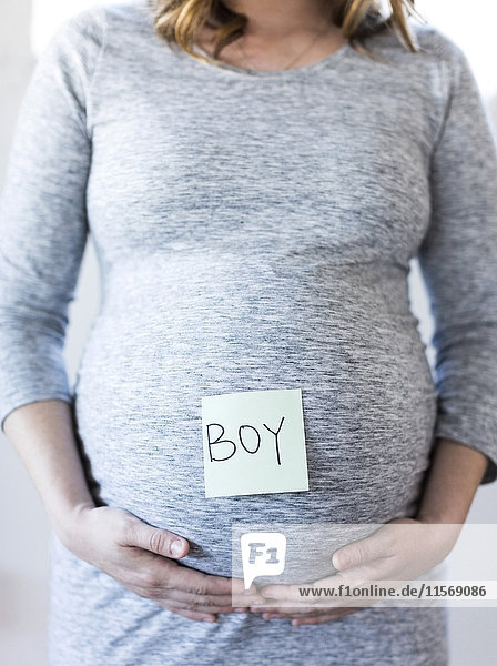 Porträt einer lächelnden schwangeren Frau mit Haftnotiz auf dem Bauch