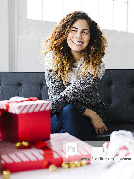 Glückliche Frau auf Sofa mit Weihnachtsgeschenken im Vordergrund