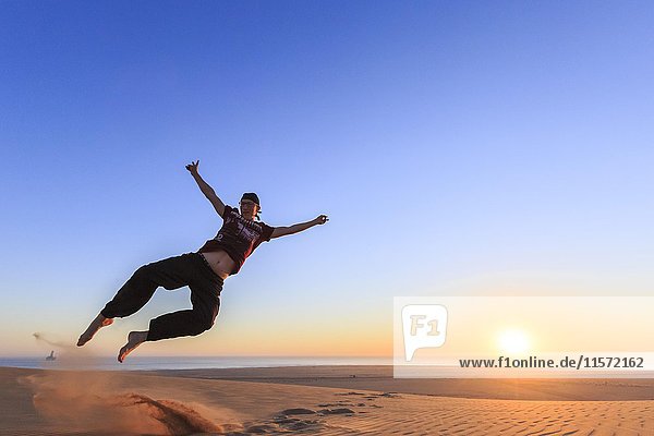 Junger Mann springt fröhlich in die Luft  Sonnenuntergang  Namib-Wüste  Langstrand  Swakopmund  Erongo-Region  Namibia  Afrika