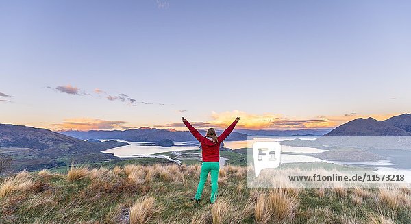 Wanderer mit ausgebreiteten Armen in der Luft  Blick auf Lake Wanaka und Berge  Sonnenuntergang  Rocky Peak  Glendhu Bay  Otago  Southland  Neuseeland  Ozeanien