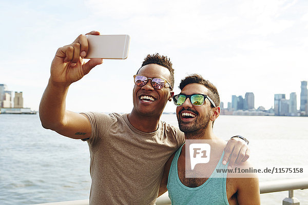 Two young men taking smartphone selfie on waterfront  New York  USA