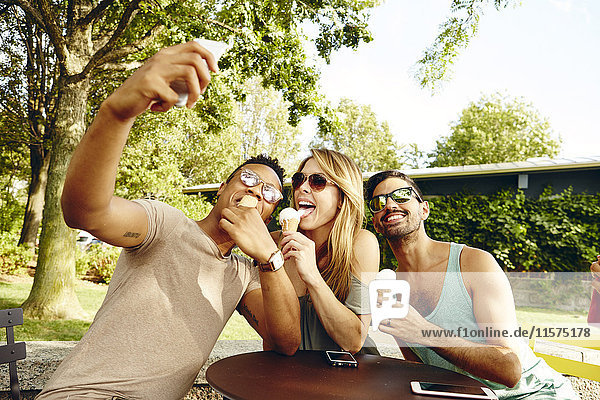Männliche und weibliche Freunde nehmen Smartphone-Selfie beim Essen von Eistüten im Park