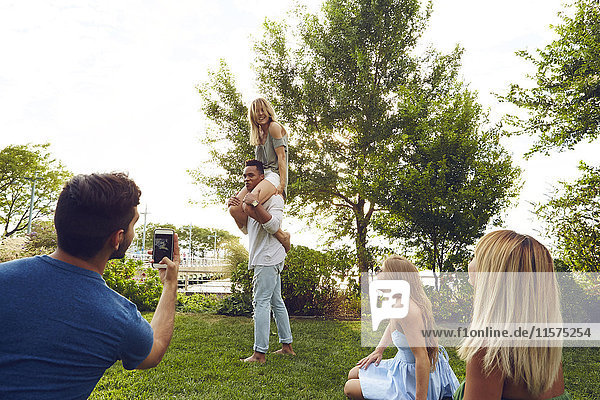 Young man photographing shoulder carrying friends in park