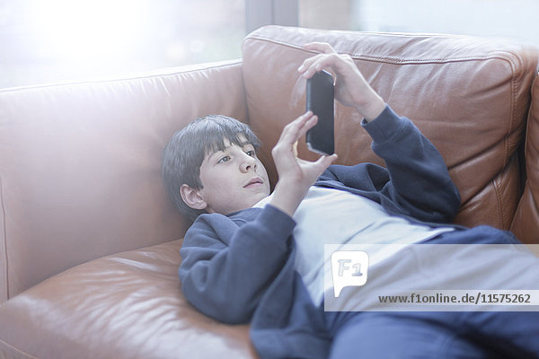 Junge spielt mit Smartphone auf dem Sofa
