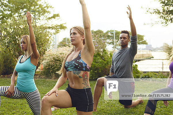 Men and women practicing yoga pose on one knee in park