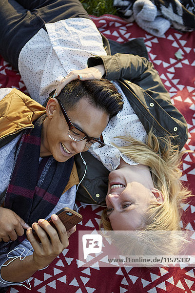 Overhead view of couple on picnic blanket sharing earphone music