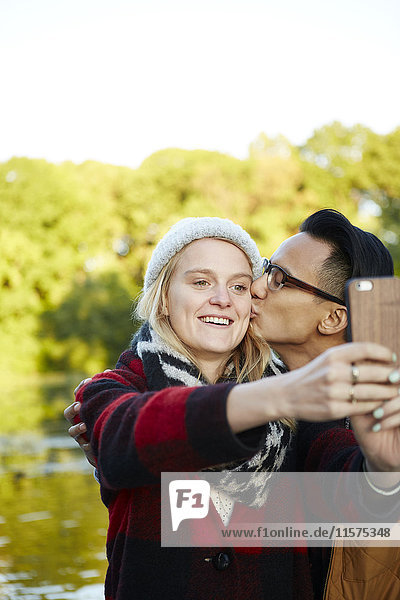 Couple taking smartphone selfie by park lakeside