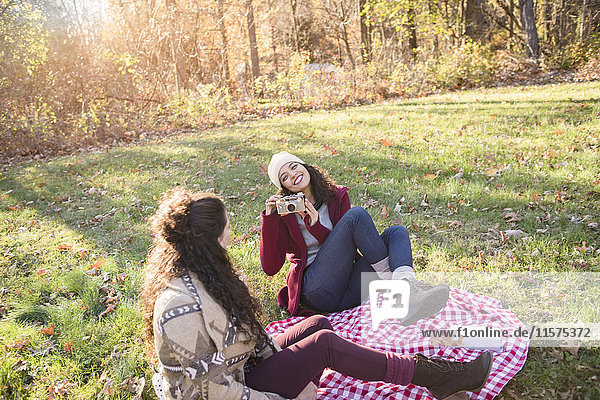 Young woman on picnic blanket photographing friend