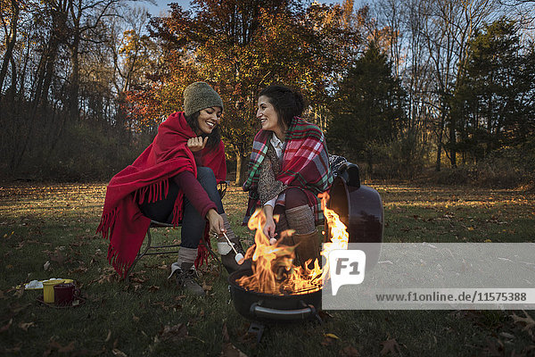 Zwei Freundinnen stoßen am Lagerfeuer auf Marshmallows an