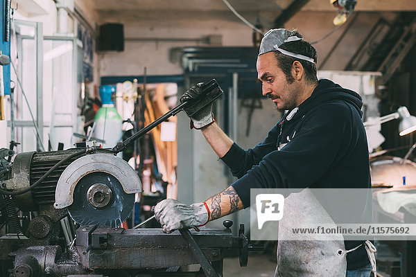 Metalworker using machine in forge workshop