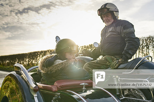 Älterer Mann und Enkel blicken von Motorrad und Beiwagen zurück