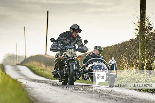 Älterer Mann und Enkel fahren Motorrad und Beiwagen entlang einer Landstraße