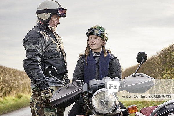 Älterer männlicher Motorradfahrer im Gespräch mit seinem auf einem Motorrad sitzenden Enkel
