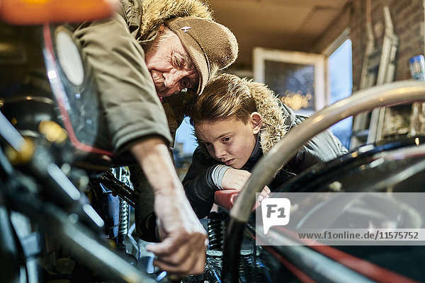 Älterer männlicher Motorradfahrer erklärt seinem Enkel in der Garage die Motorrad-Wartung