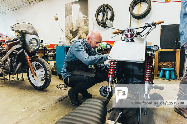 Älterer Mann  der in der Werkstatt am Motorrad arbeitet