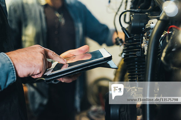 Zwei reife Männer  die in einer Garage arbeiten und ein digitales Tablet benutzen  Nahaufnahme
