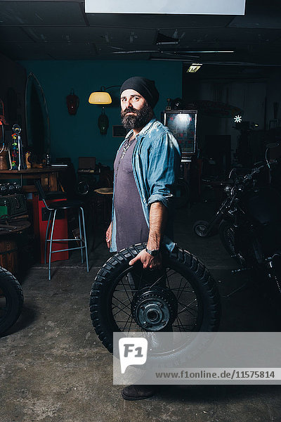 Porträt eines reifen Mannes in der Garage  der einen Motorradreifen hält