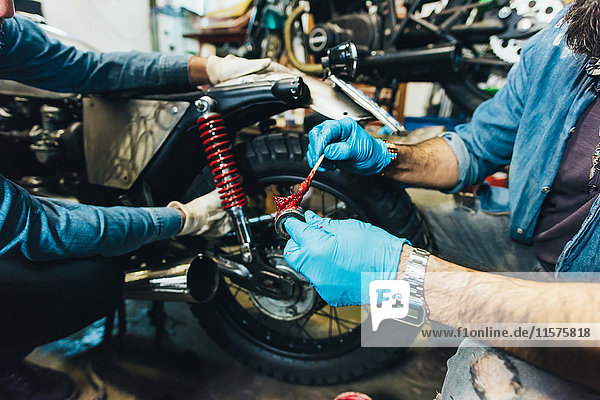Zwei reife Männer  die in der Garage auf einem Motorrad arbeiten  Nahaufnahme