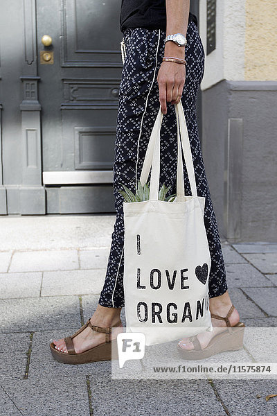 Waist down view of woman strolling on street carrying organic shopping bag