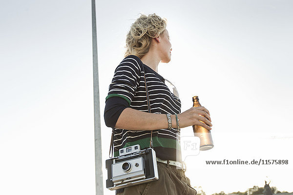 Mid adult woman carrying beer bottle and vintage camera in park