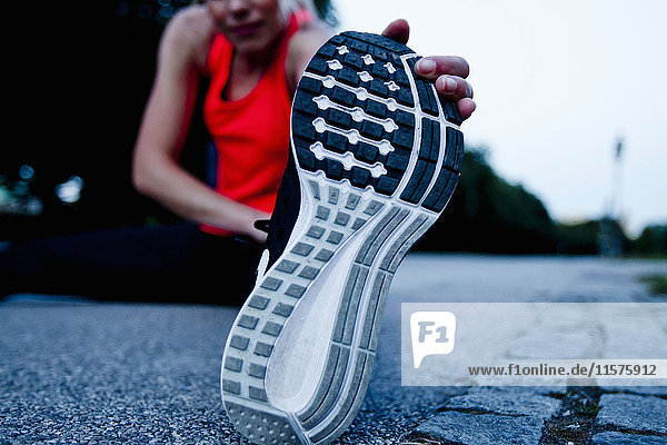 Surface level view of woman training  touching sole of training shoe in park at dusk