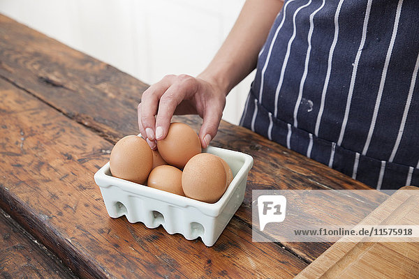 Frau pickt mit der Hand ein Ei vom Karton auf der Küchentheke