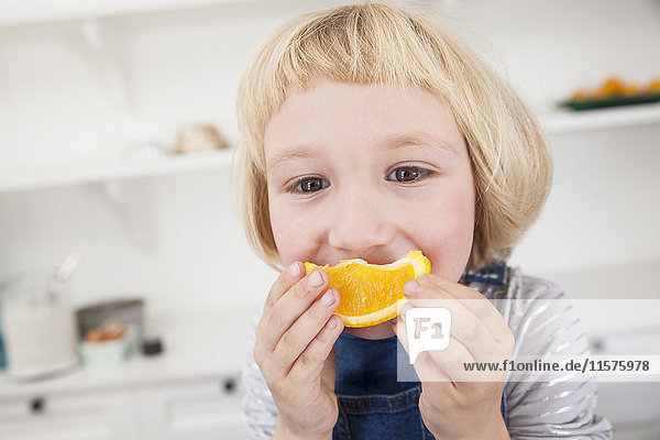 Portrait of cute girl in kitchen holding orange slice to her mouth