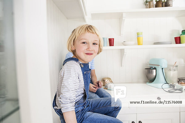 Porträt eines niedlichen Mädchens  das vor seinem Bruder auf dem Küchentisch sitzt