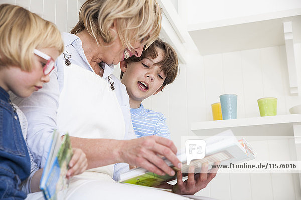 Mature woman sitting on kitchen counter reading storybooks with son and daughter