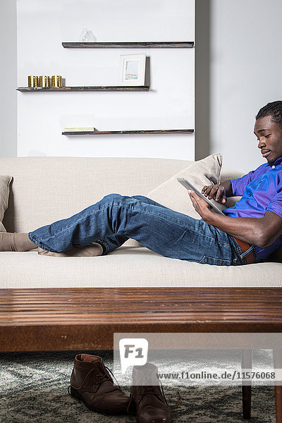 Junger Mann entspannt auf dem Sofa  mit digitalem Tablett