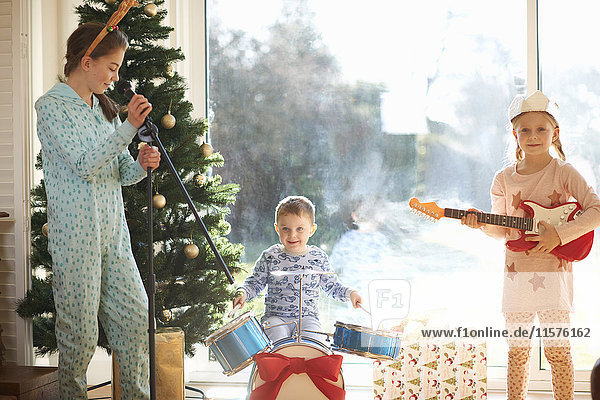 Junge und Schwestern spielen Spielzeug-Schlagzeug und Gitarre am Weihnachtstag