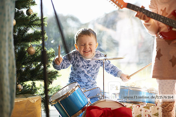 Junge und Schwester spielen am Weihnachtstag Spielzeug-Schlagzeug und Gitarre